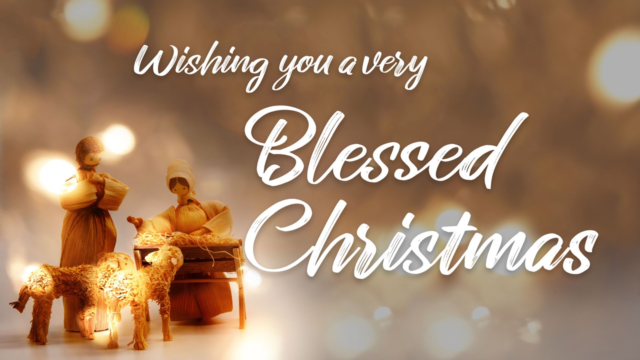 Stock image of a Nativity scene made with corn husk dolls, with the words "Wishing You A Very Blessed Christmas" displayed