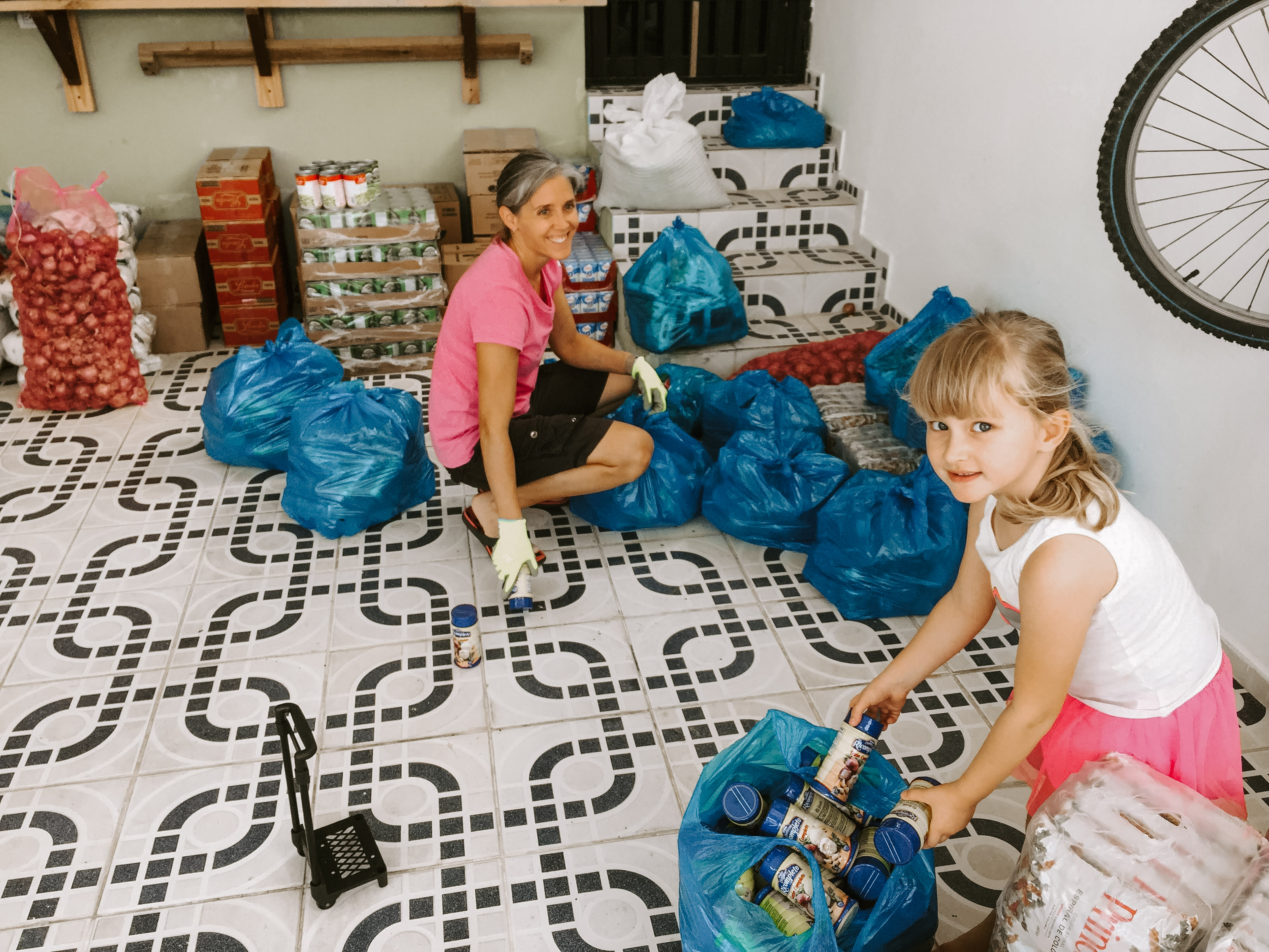 DeWeerd Three Heather and little girl helping package canned food for locals.
