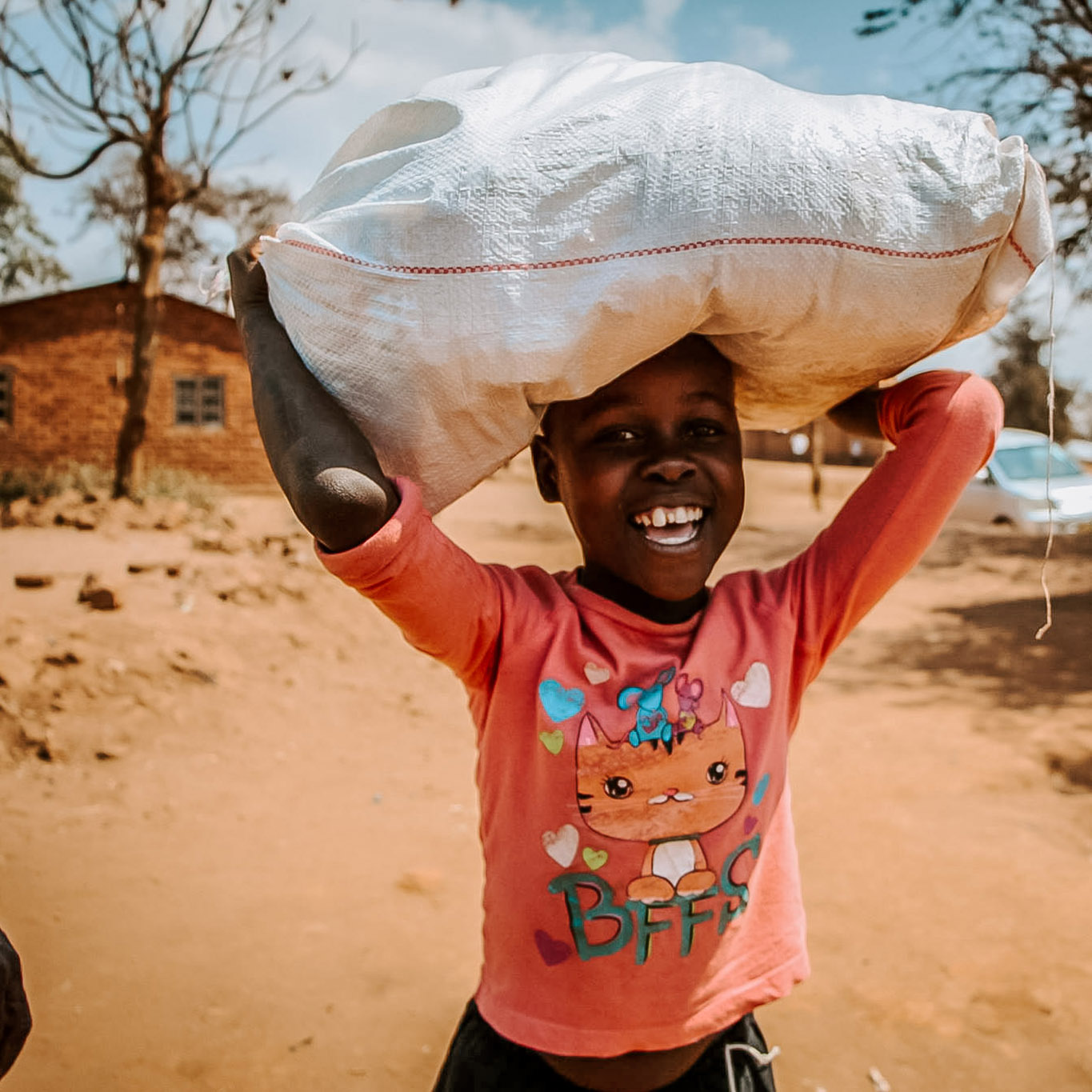 Photo of a little girl from Villages of Hope Africa holding a bag on her head