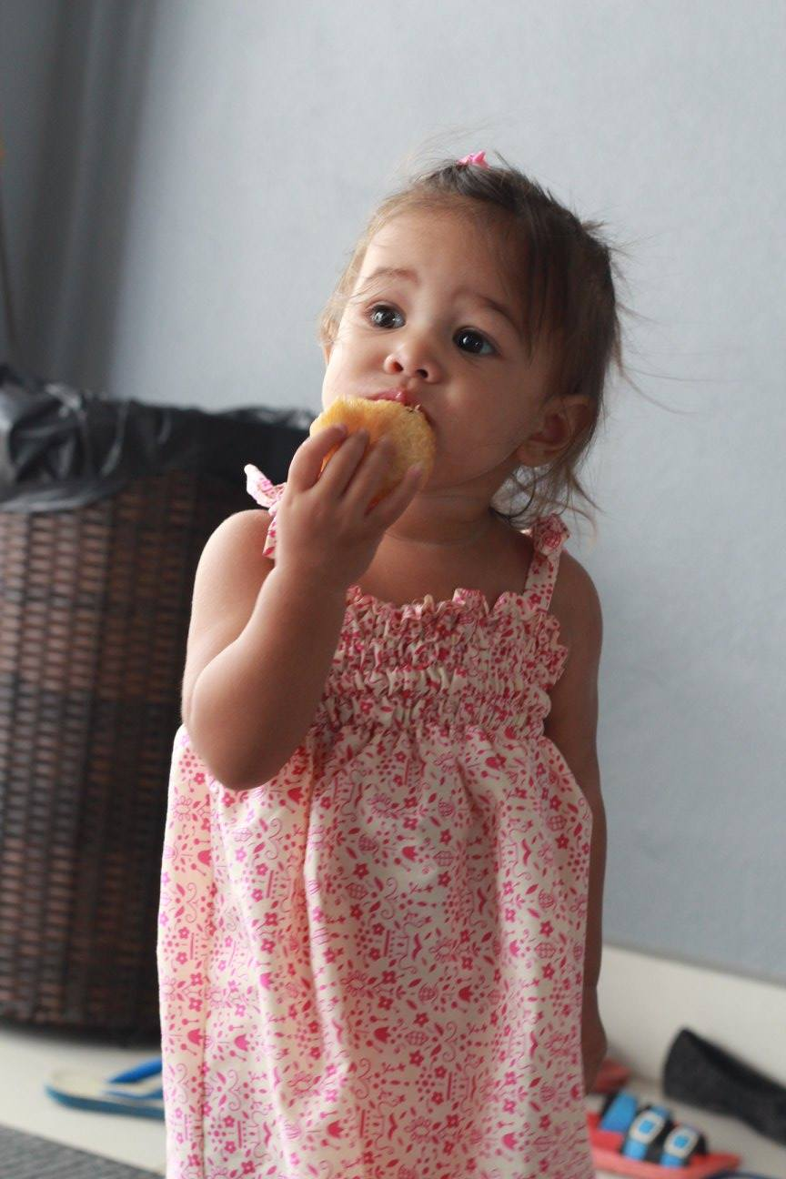Photo of a little girl in a red dotted dress eating.