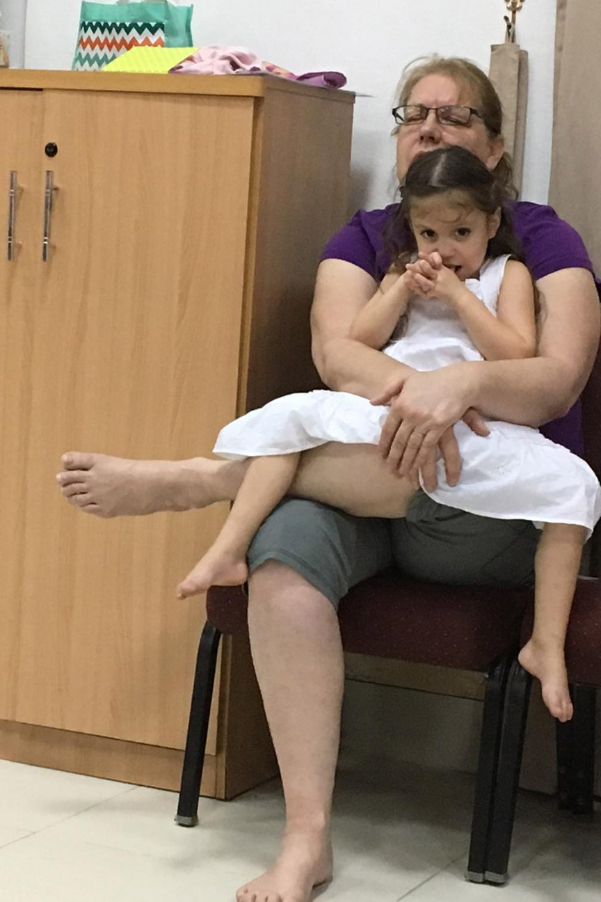 Photo of a girl and her mom sitting on a chair, with the girl looking at the camera.